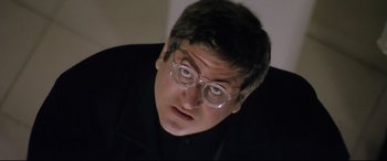 Movie still from “Anguish” (1987), directed by Bigas Luna – A person wearing glasses and a black shirt; Close Up shot, Low angle