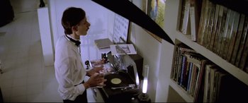 Movie still from “Anguish” (1987), directed by Bigas Luna – A man standing in front of a record player; Medium shot, Low angle