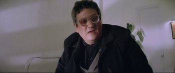 Movie still from “Anguish” (1987), directed by Bigas Luna – A man in a black jacket is sitting down; Close Up shot, Low angle