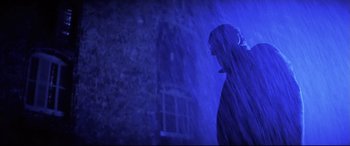 Movie still from “Anguish” (1987), directed by Bigas Luna – A man standing in the rain with a blue light behind him; Medium shot, Low angle