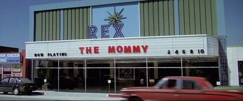 Movie still from “Anguish” (1987), directed by Bigas Luna – A red truck driving past a movie theater; Extreme Wide shot, Low angle