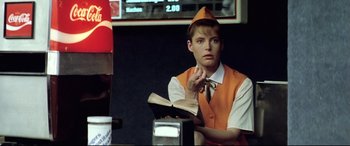 Movie still from “Anguish” (1987), directed by Bigas Luna – A woman in an orange vest holding an open book; Medium shot, Low angle