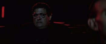 Movie still from “Anguish” (1987), directed by Bigas Luna – A man with glasses is sitting in a dark room; Close Up shot, Low angle