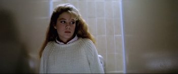 Movie still from “Anguish” (1987), directed by Bigas Luna – A young woman in a white sweater is standing in front of a wall; Close Up shot, Low angle