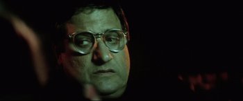 Movie still from “Anguish” (1987), directed by Bigas Luna – A person wearing glasses with a dark background; Close Up shot, Over the shoulder angle