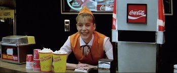 Movie still from “Anguish” (1987), directed by Bigas Luna – A young man sitting at a table in front of a drink; Medium shot, Low angle