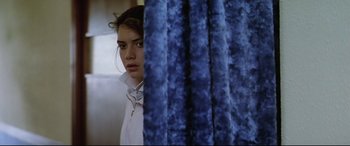 Movie still from “Anguish” (1987), directed by Bigas Luna – A young woman standing next to a blue curtain; Close Up shot, Over the shoulder angle
