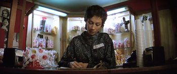 Movie still from “Anguish” (1987), directed by Bigas Luna – A woman sitting at a counter writing on a piece of paper; Medium shot, Low angle