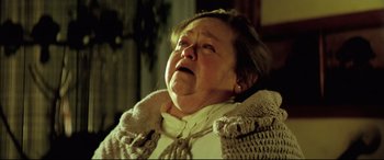 Movie still from “Anguish” (1987), directed by Bigas Luna – An older woman is crying while sitting in a chair; Close Up shot, Low angle