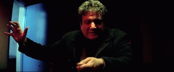 Movie still from “Anguish” (1987), directed by Bigas Luna – A man sitting in a dark room with his hands crossed; Close Up shot, Low angle