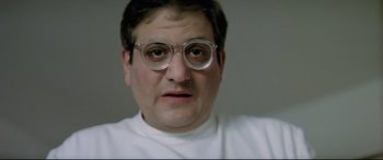 Movie still from “Anguish” (1987), directed by Bigas Luna – A person wearing glasses and a white shirt; Close Up shot, Low angle