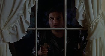 Movie still from “National Lampoon's Animal House” (1978), directed by John Landis – A man holding a cell phone in front of a window; Medium shot, Low angle