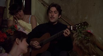 Movie still from “National Lampoon's Animal House” (1978), directed by John Landis – A man playing a guitar while sitting on the floor; Medium shot, Over the shoulder angle