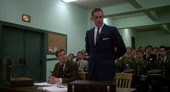 Movie still from “National Lampoon's Animal House” (1978), directed by John Landis – A man in a suit standing in front of a briefcase in a courtroom; Medium shot, Low angle