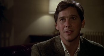 Movie still from “National Lampoon's Animal House” (1978), directed by John Landis – A man in a suit and tie sitting in front of a lamp; Close Up shot, Over the shoulder angle