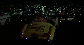 Movie still from “National Lampoon's Animal House” (1978), directed by John Landis – A man standing on the hood of a yellow car at night; Extreme Wide shot, High angle