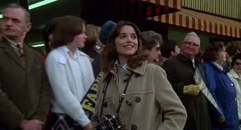 Movie still from “National Lampoon's Animal House” (1978), directed by John Landis – A woman in a brown coat holding a camera and smiling; Close Up shot, Low angle