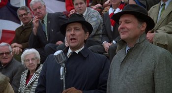 Movie still from “National Lampoon's Animal House” (1978), directed by John Landis – A man in a black hat and a microphone in front of a group of people; Medium shot, Low angle