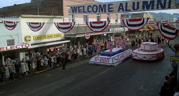 Movie still from “National Lampoon's Animal House” (1978), directed by John Landis – A parade float with an image of president bill clinton on it; Extreme Wide shot, High angle