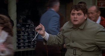 Movie still from “National Lampoon's Animal House” (1978), directed by John Landis – A man in a trench coat holding a wii controller; Close Up shot, Low angle