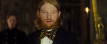 Movie still from “Anna Karenina” (2012), directed by Joe Wright – A man with long red hair wearing a suit and bow tie; Close Up shot, Low angle