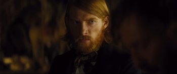 Movie still from “Anna Karenina” (2012), directed by Joe Wright – A man with long red hair wearing a suit and bow tie; Close Up shot, Over the shoulder angle