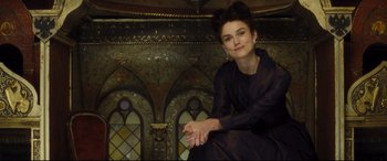 Movie still from “Anna Karenina” (2012), directed by Joe Wright – A woman sitting on a chair in front of an ornate wall; Medium shot, Low angle