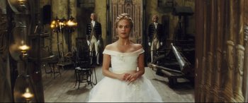Movie still from “Anna Karenina” (2012), directed by Joe Wright – A woman in a white dress sitting in front of two other men; Medium shot, Over the shoulder angle