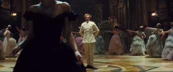 Movie still from “Anna Karenina” (2012), directed by Joe Wright – A man in a white suit standing in front of a group of people; Wide shot, Over the shoulder angle