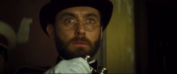 Movie still from “Anna Karenina” (2012), directed by Joe Wright – A person wearing glasses and a hat; Close Up shot, Low angle