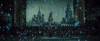 Movie still from “Anna Karenina” (2012), directed by Joe Wright – A snowy scene of a city with a person sitting on a bench in front of it; Extreme Wide shot, Low angle