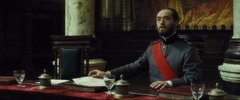 Movie still from “Anna Karenina” (2012), directed by Joe Wright – A man sitting at a table in front of papers; Medium shot, Low angle