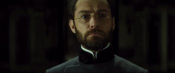 Movie still from “Anna Karenina” (2012), directed by Joe Wright – A person wearing a suit and glasses; Close Up shot, Low angle