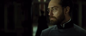 Movie still from “Anna Karenina” (2012), directed by Joe Wright – A person wearing glasses and a suit; Close Up shot, Over the shoulder angle