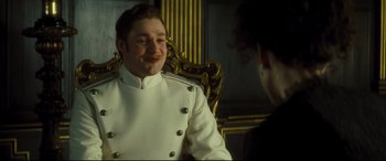 Movie still from “Anna Karenina” (2012), directed by Joe Wright – A man in a white jacket sitting in a chair; Medium shot, Over the shoulder angle