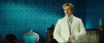 Movie still from “Anna Karenina” (2012), directed by Joe Wright – A man in a white suit standing next to a chair; Medium shot, Over the shoulder angle