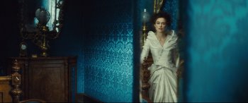 Movie still from “Anna Karenina” (2012), directed by Joe Wright – A woman in a white dress sitting on a chair; Medium shot, Over the shoulder angle