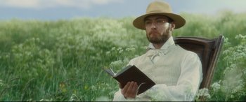 Movie still from “Anna Karenina” (2012), directed by Joe Wright – A man in a hat and glasses holding a book; Medium shot, Low angle