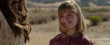 Movie still from “Annabelle: Creation” (2017), directed by David F. Sandberg – A young girl smiling for the camera in a field; Close Up shot, Over the shoulder angle