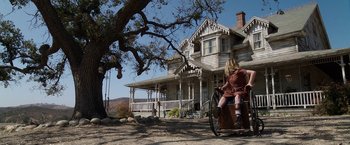 Movie still from “Annabelle: Creation” (2017), directed by David F. Sandberg – A woman riding a bike in front of an old house; Wide shot, Low angle