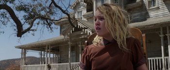 Movie still from “Annabelle: Creation” (2017), directed by David F. Sandberg – A young girl with blonde hair is standing in front of an old house; Medium shot, Low angle