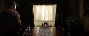 Movie still from “Annabelle: Creation” (2017), directed by David F. Sandberg – A doll sitting on top of a table in front of a window; Wide shot, High angle