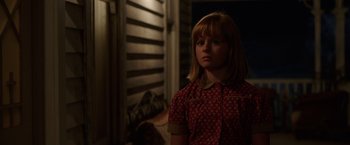 Movie still from “Annabelle: Creation” (2017), directed by David F. Sandberg – A young girl in a red shirt is standing in front of a wooden wall; Close Up shot, Over the shoulder angle