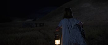 Movie still from “Annabelle: Creation” (2017), directed by David F. Sandberg – A woman holding a lantern in a field at night; Medium shot, Over the shoulder angle