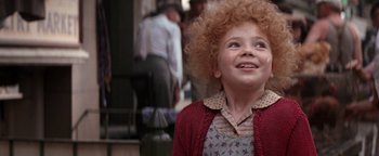 Movie still from “Annie” (1982), directed by John Huston – A young girl with a curly red hair is smiling for the camera; Close Up shot, High angle