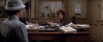 Movie still from “Annie” (1982), directed by John Huston – A woman sitting at a desk in front of papers; Medium shot, High angle