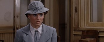 Movie still from “Annie” (1982), directed by John Huston – A woman wearing a suit and a hat in front of a wall; Close Up shot, Over the shoulder angle