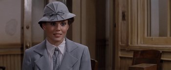 Movie still from “Annie” (1982), directed by John Huston – A woman wearing a suit and a hat in front of a wall; Close Up shot, Over the shoulder angle