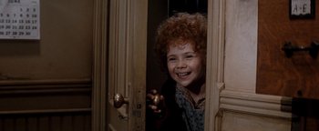 Movie still from “Annie” (1982), directed by John Huston – A young girl smiling and holding a door knob; Close Up shot, High angle