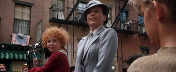 Movie still from “Annie” (1982), directed by John Huston – A woman wearing a hat and a suit standing next to another woman in front of a building; Close Up shot, Over the shoulder angle